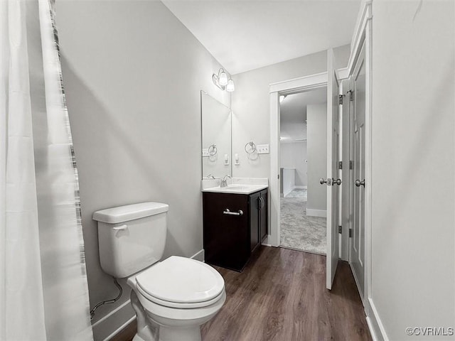 bathroom with vanity, toilet, wood finished floors, and baseboards