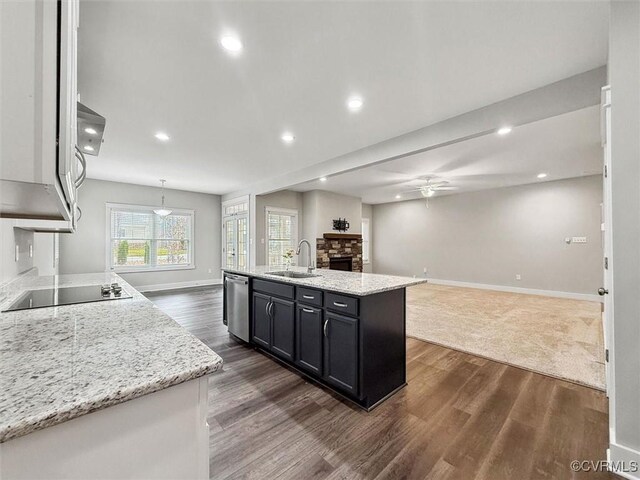 kitchen with a sink, stainless steel dishwasher, open floor plan, a stone fireplace, and black electric stovetop