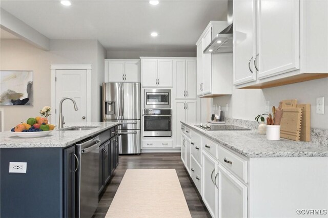 kitchen with an island with sink, a sink, stainless steel appliances, white cabinetry, and wall chimney exhaust hood