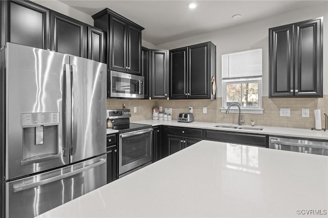 kitchen with a sink, dark cabinetry, decorative backsplash, and stainless steel appliances