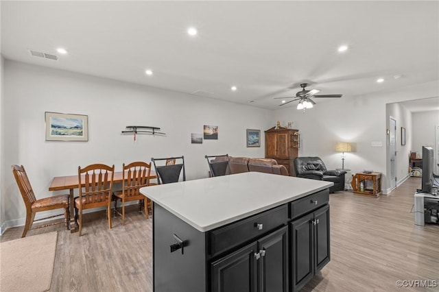 kitchen with visible vents, a kitchen island, dark cabinetry, and light wood finished floors