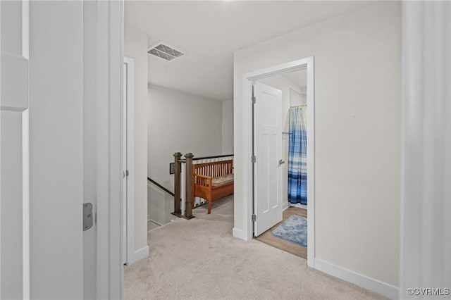 corridor with visible vents, an upstairs landing, light colored carpet, and baseboards