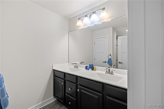 full bathroom with double vanity, wood finished floors, baseboards, and a sink