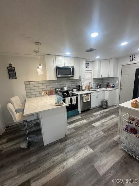 kitchen featuring a peninsula, a sink, light countertops, appliances with stainless steel finishes, and white cabinetry