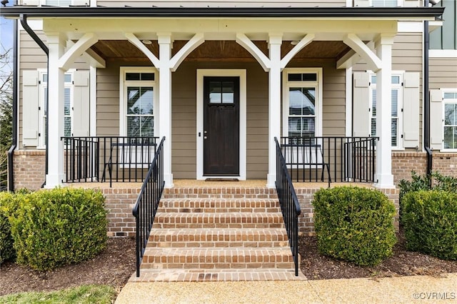 view of exterior entry with brick siding and covered porch