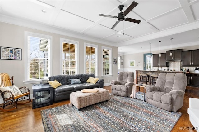 living room featuring ornamental molding, a ceiling fan, coffered ceiling, wood finished floors, and baseboards