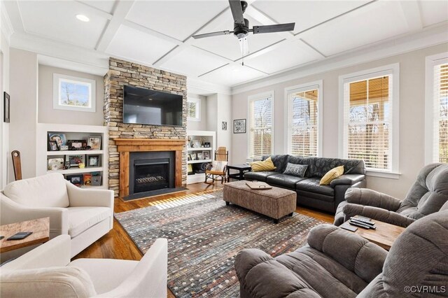 living area with ornamental molding, coffered ceiling, wood finished floors, a stone fireplace, and ceiling fan