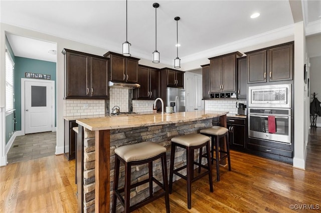 kitchen featuring dark wood finished floors, dark brown cabinets, a kitchen breakfast bar, and stainless steel appliances