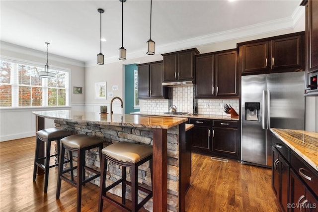 kitchen with light stone countertops, appliances with stainless steel finishes, a breakfast bar, and wood finished floors