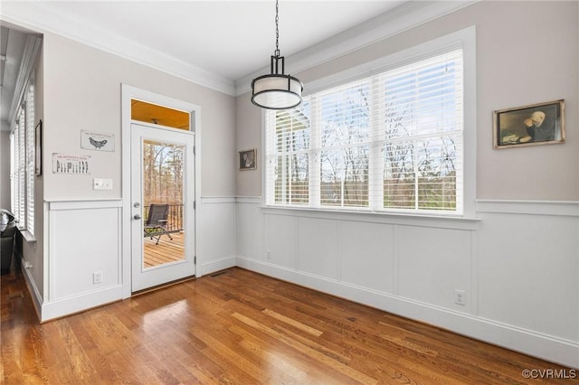 unfurnished dining area with wood finished floors, a wainscoted wall, a wealth of natural light, and ornamental molding