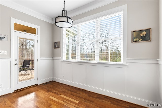 unfurnished dining area featuring visible vents, wood finished floors, a wainscoted wall, and ornamental molding