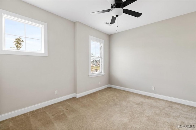 empty room with light colored carpet, a ceiling fan, and baseboards