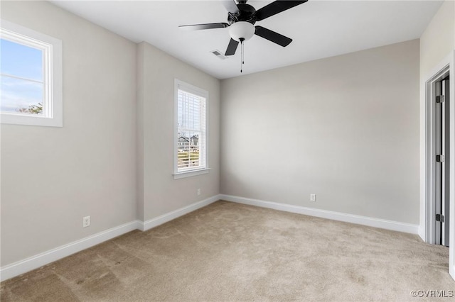 spare room featuring visible vents, light colored carpet, a ceiling fan, and baseboards