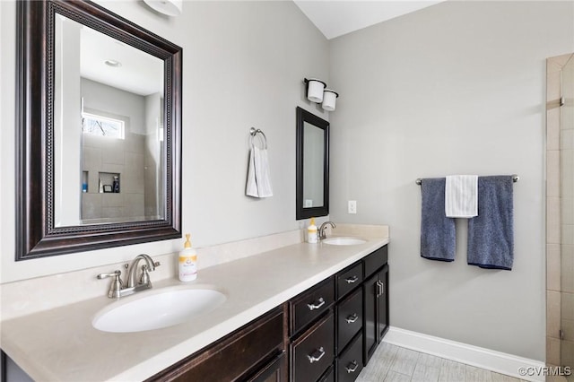 full bathroom featuring double vanity, tiled shower, baseboards, and a sink