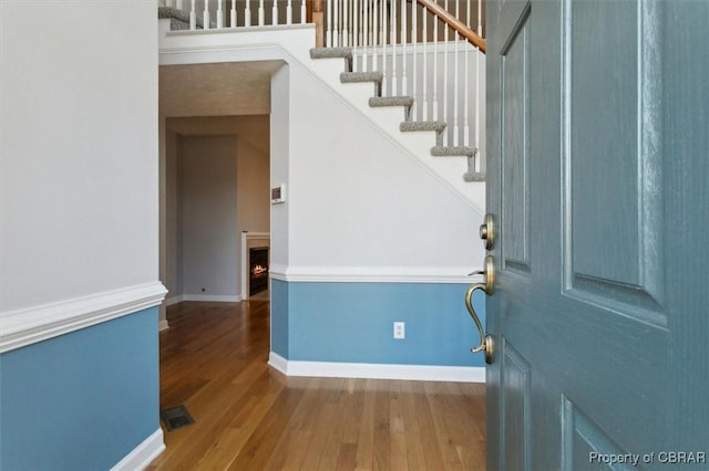 foyer featuring stairway, wood finished floors, visible vents, baseboards, and a lit fireplace