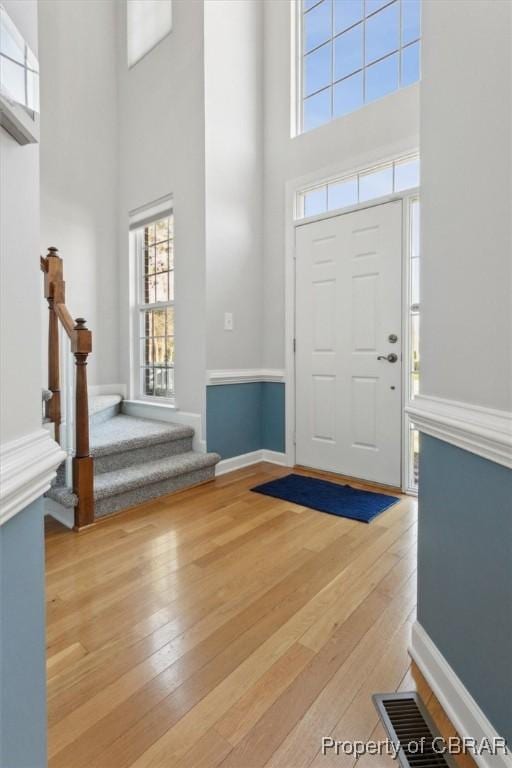 entryway with visible vents, stairway, light wood-style floors, and a towering ceiling