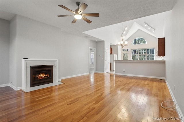 unfurnished living room with a fireplace with flush hearth, ceiling fan with notable chandelier, light wood-type flooring, and baseboards