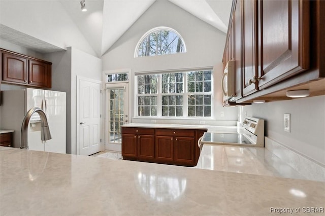 kitchen with light stone counters, white microwave, high vaulted ceiling, stove, and fridge with ice dispenser