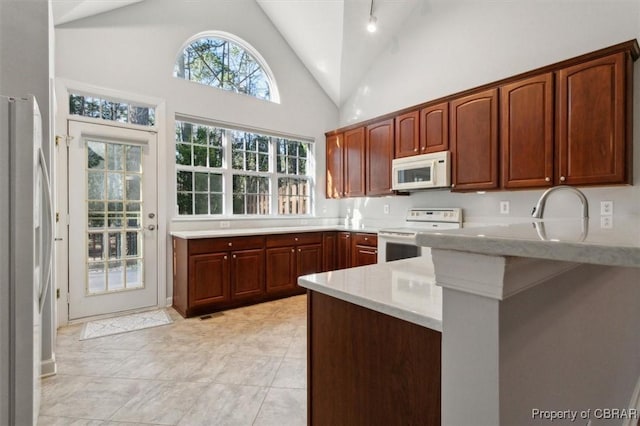 kitchen featuring light tile patterned floors, a peninsula, white appliances, high vaulted ceiling, and a sink