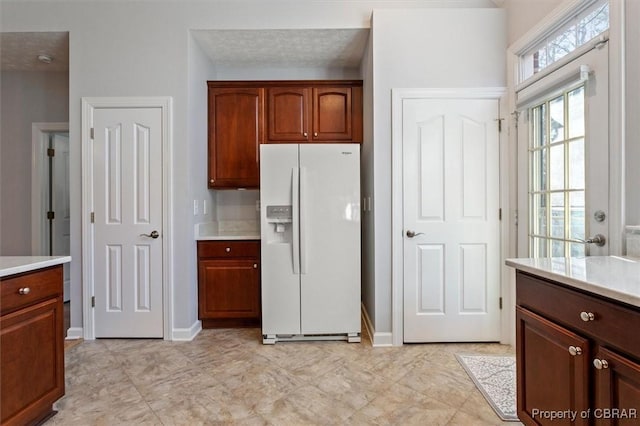 kitchen with baseboards, white refrigerator with ice dispenser, and light countertops