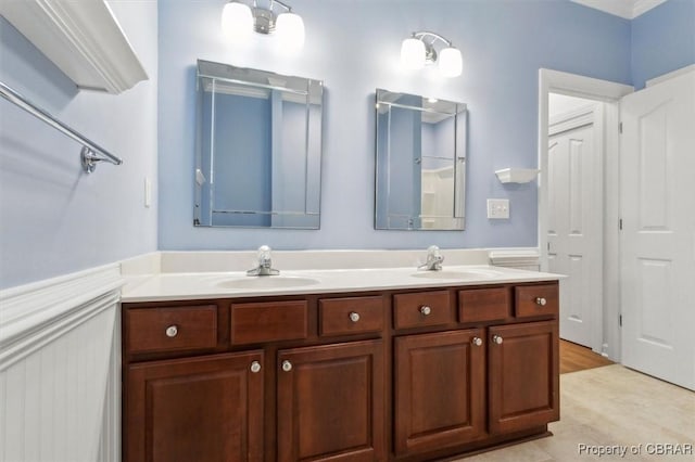 full bath with a sink, double vanity, and wainscoting