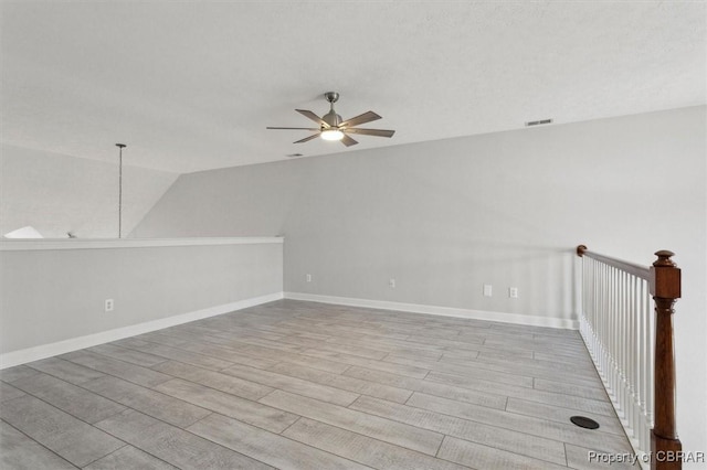 spare room with light wood-type flooring, visible vents, lofted ceiling, baseboards, and ceiling fan