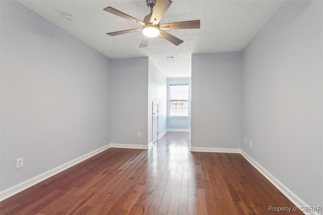 empty room featuring visible vents, a ceiling fan, dark wood-type flooring, and baseboards