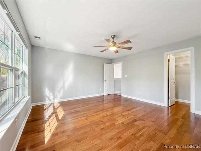 empty room featuring light wood finished floors, visible vents, a ceiling fan, and baseboards