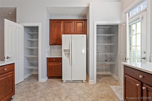 kitchen featuring baseboards, white refrigerator with ice dispenser, and light countertops