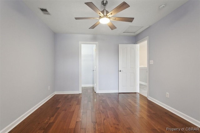 empty room featuring baseboards, visible vents, attic access, ceiling fan, and dark wood-type flooring