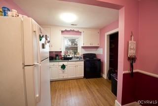 kitchen featuring stove, white cabinets, freestanding refrigerator, and wood finished floors