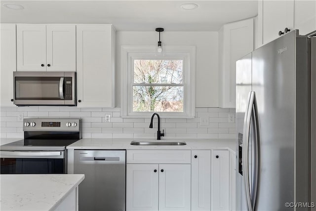 kitchen featuring a sink, backsplash, white cabinetry, stainless steel appliances, and light stone countertops