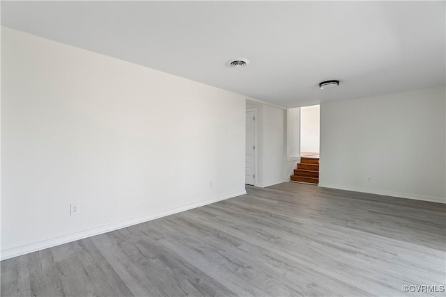 empty room with stairway, baseboards, visible vents, and wood finished floors