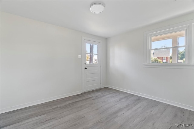 unfurnished room featuring wood finished floors, a healthy amount of sunlight, and baseboards