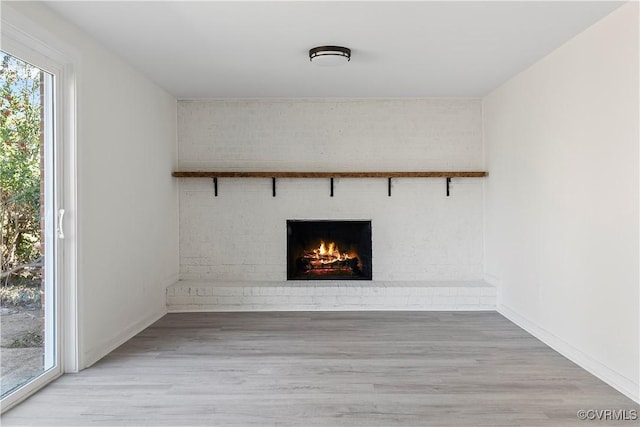 unfurnished living room featuring baseboards, a brick fireplace, and wood finished floors