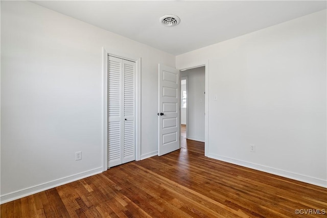 unfurnished bedroom featuring visible vents, baseboards, a closet, and wood finished floors