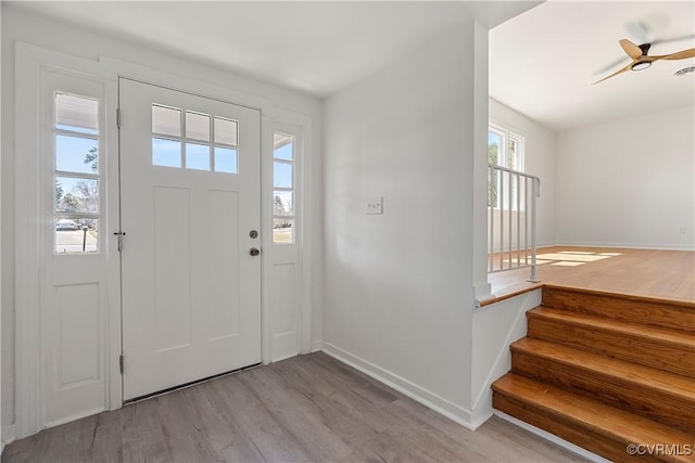 foyer featuring stairway, a ceiling fan, visible vents, baseboards, and light wood-type flooring