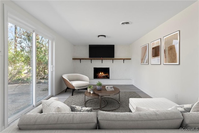 living area featuring visible vents, a brick fireplace, baseboards, and wood finished floors