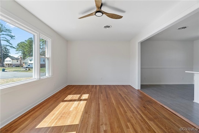 empty room with ceiling fan, visible vents, baseboards, and wood finished floors