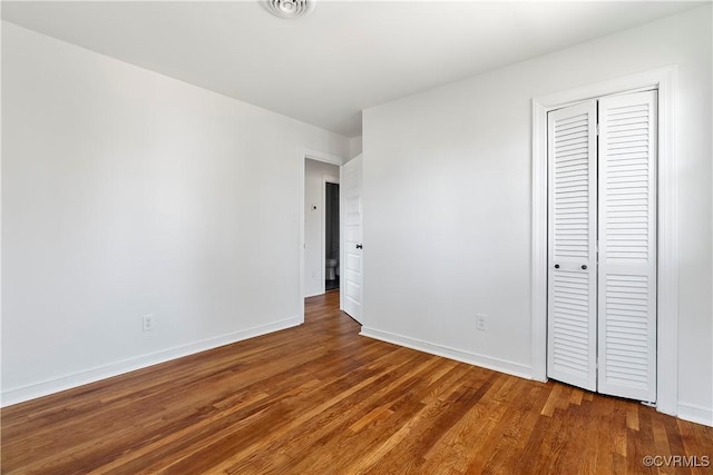 unfurnished bedroom with a closet, visible vents, baseboards, and wood finished floors