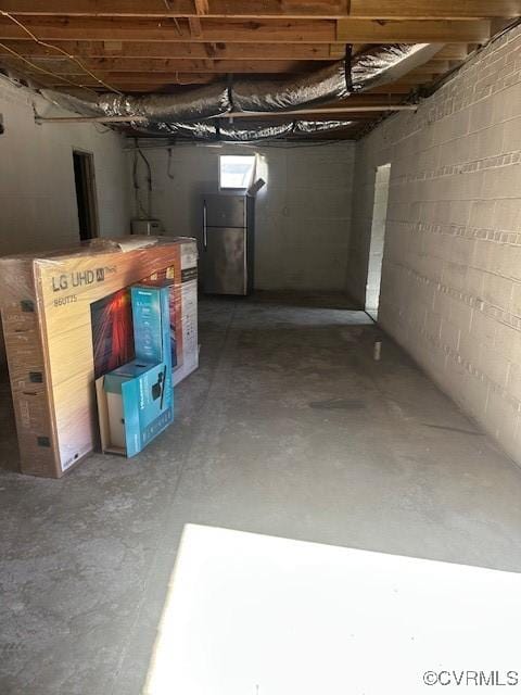 unfinished below grade area with concrete block wall and freestanding refrigerator