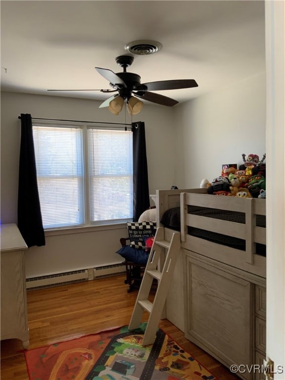 bedroom featuring light wood finished floors, multiple windows, and a baseboard radiator