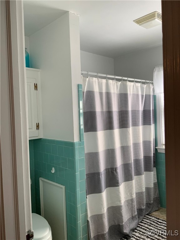 bathroom with visible vents, curtained shower, a wainscoted wall, toilet, and tile walls