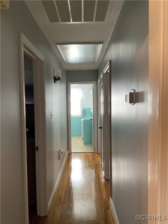 hallway featuring visible vents, attic access, baseboards, and wood-type flooring