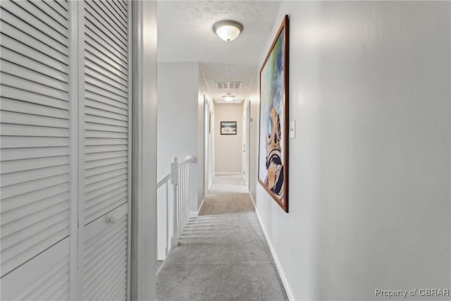 hallway with baseboards, carpet, visible vents, and a textured ceiling