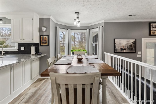 dining room with crown molding, light wood-style floors, visible vents, and a textured ceiling