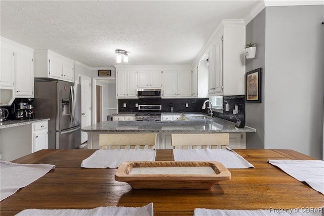 kitchen with a sink, backsplash, appliances with stainless steel finishes, white cabinets, and a peninsula