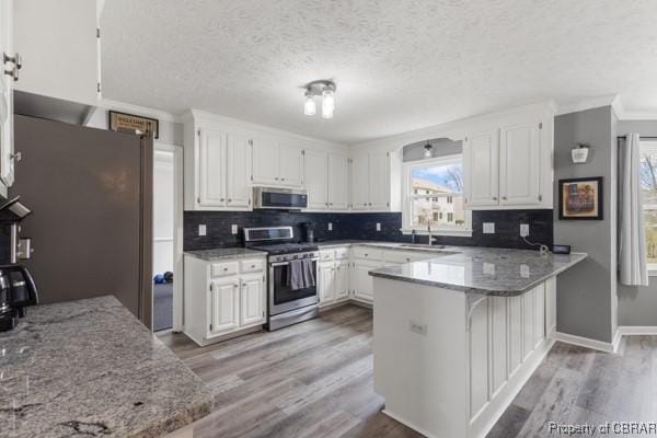 kitchen featuring light wood finished floors, appliances with stainless steel finishes, white cabinetry, and a peninsula