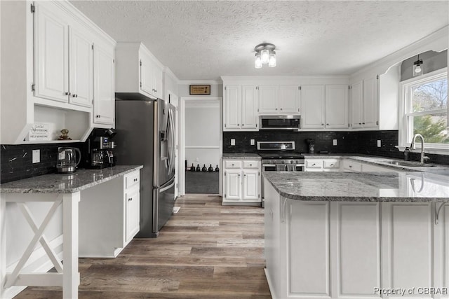 kitchen featuring light stone counters, a sink, stainless steel appliances, white cabinets, and light wood-style floors