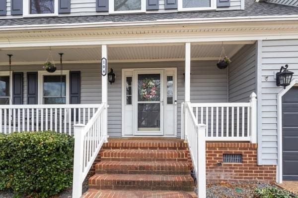 property entrance featuring a porch, a garage, roof with shingles, and brick siding